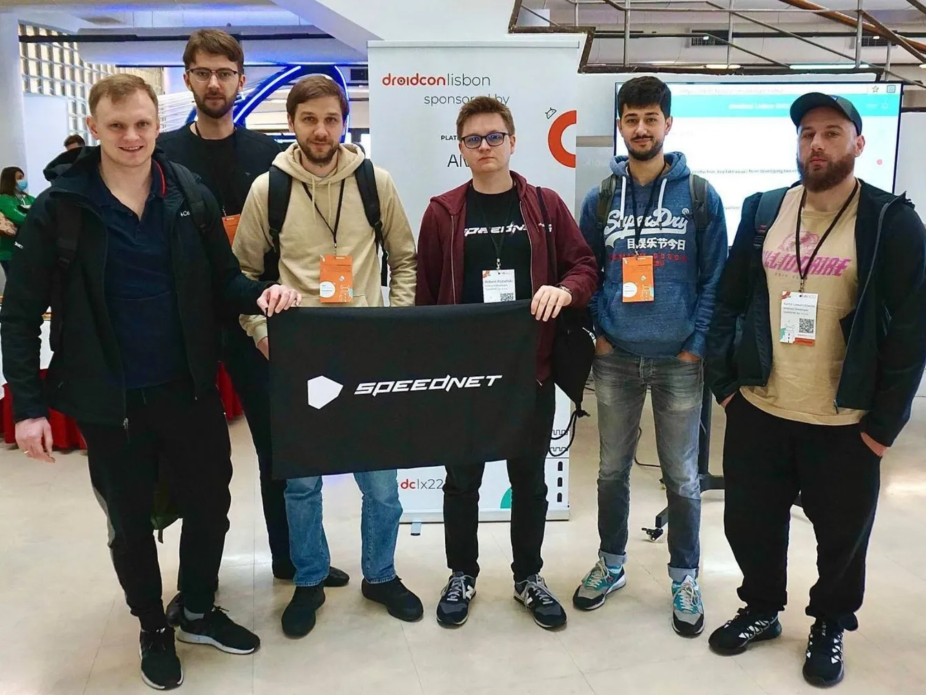 Zespół trzyma baner Speednet w hali konferencji Droidcon Lisbon.