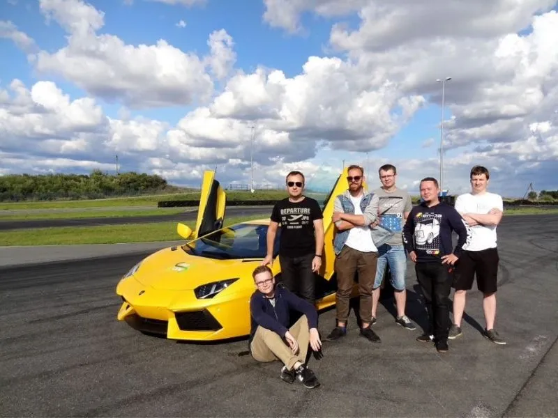 Sześcioro pracowników pozuje przy żółtym Lamborghini na torze wyścigowym podczas eventu firmowego.