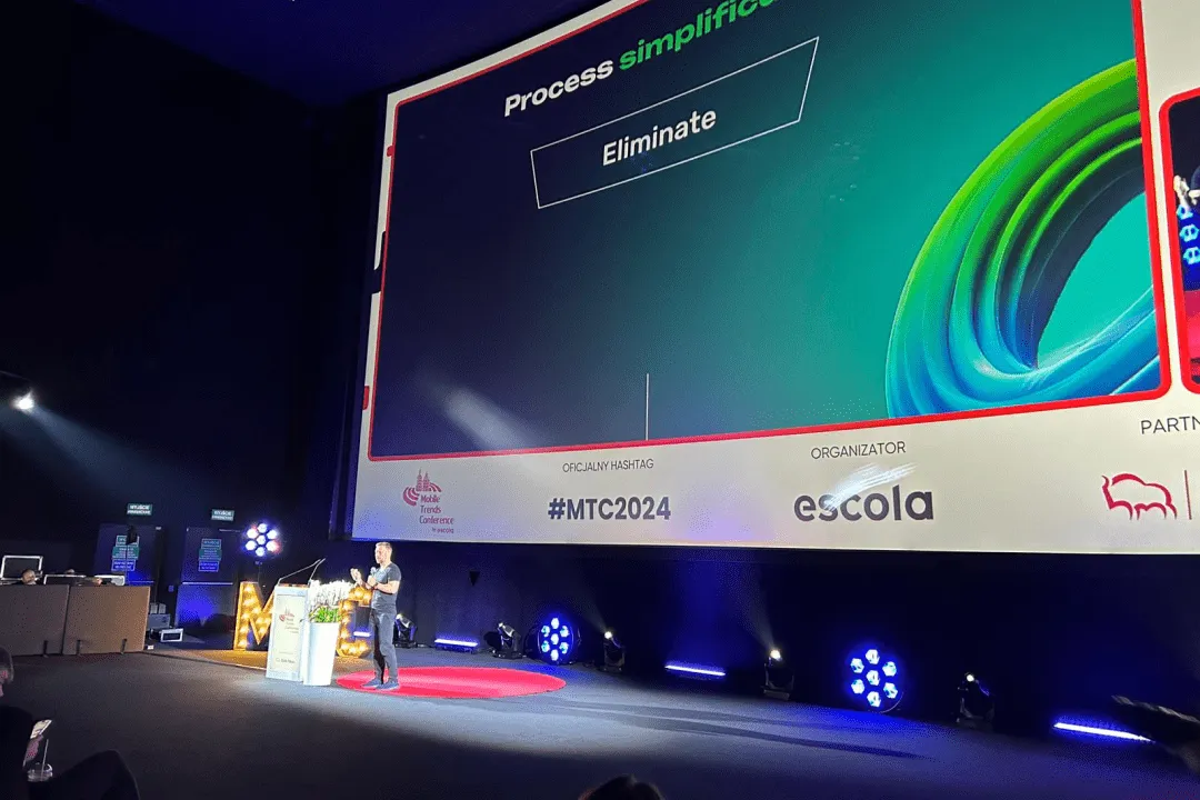 Conference stage with a screen reading 'Process simplification' and 'Eliminate', under the hashtag #MTC2024.