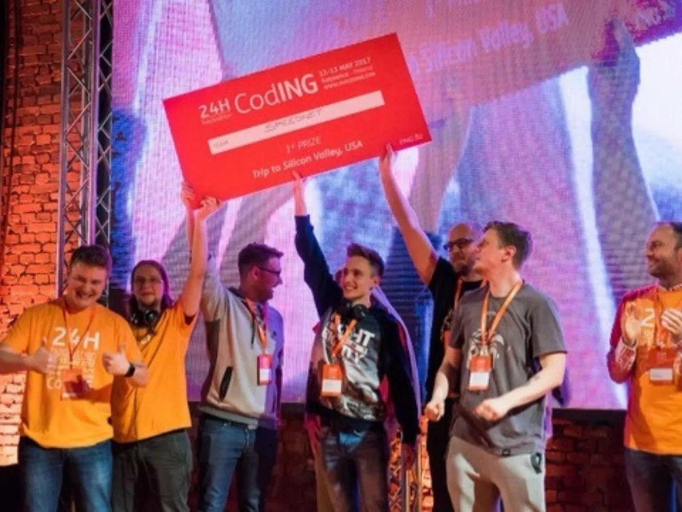 Zespół na scenie trzyma czek z hackathonu 24H CodING: 1. miejsce i nagroda w postaci wyjazdu do Doliny Krzemowej w USA.