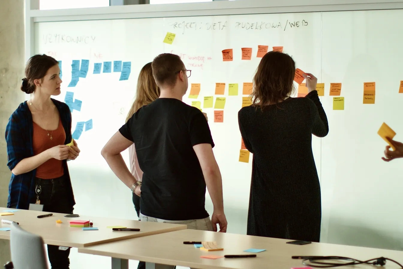 Zespół rozkłada kolorowe karteczki na tablicy z napisem "Projekt: Dieta pudełkowa/Web" podczas warsztatu User Story Mapping.