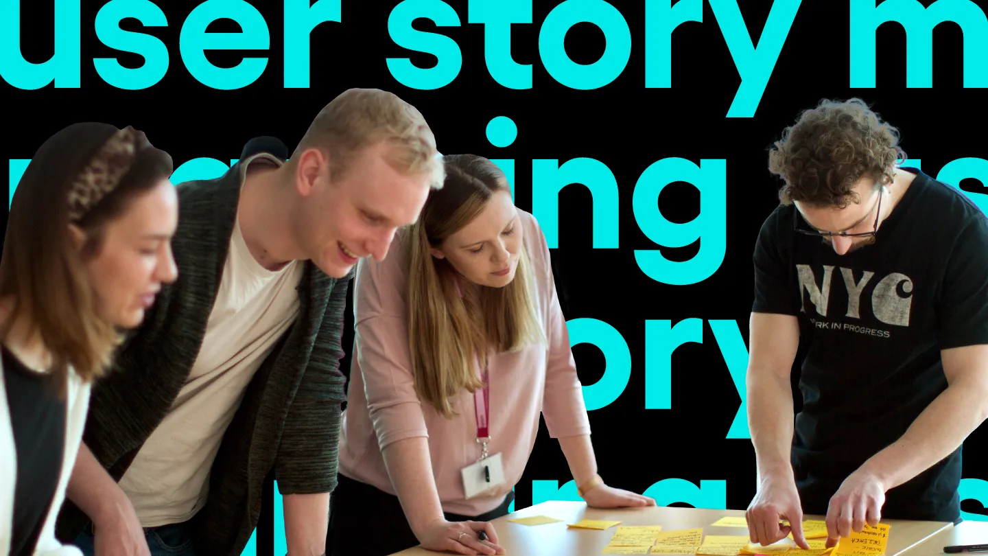 Czworo pracowników pochylonych nad stołem z karteczkami samoprzylepnymi, na tle napisu "user story mapping".