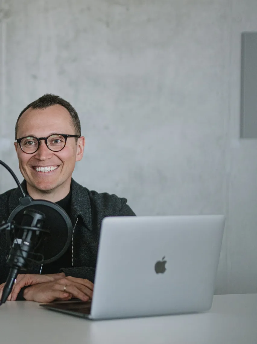 A smiling Speednet team member at a laptop with a studio microphone.