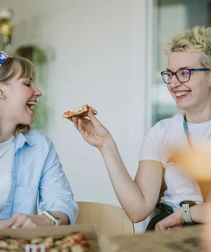 Two Speednet team members laughing and sharing pizza at a table.