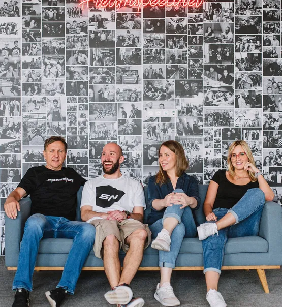 Four Speednet team members laughing on a couch in front of the photo wall.