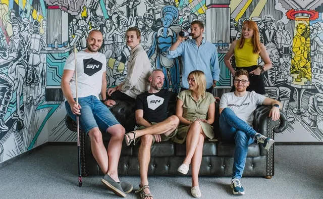 The Speednet team gathered on a leather couch in front of a mural.